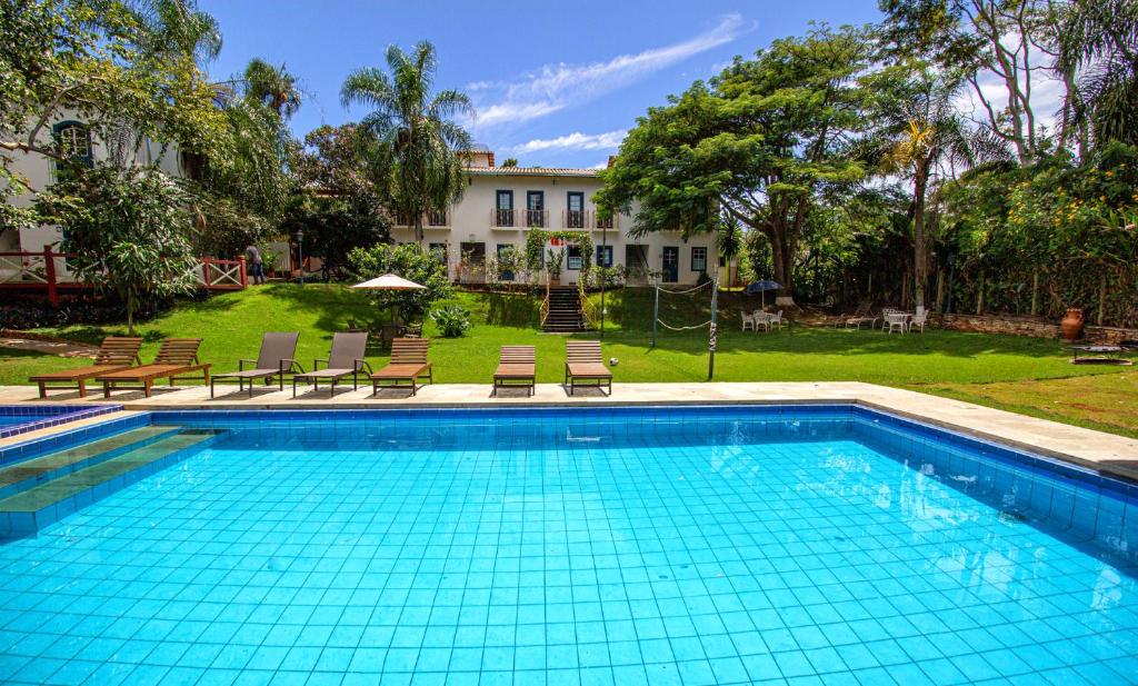 a swimming pool with chairs and a house in the background at Pousada Villa Bia in Pirenópolis