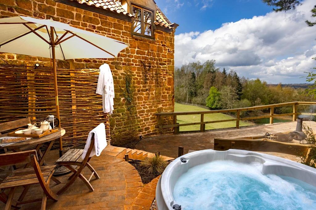 a hot tub on a patio with a table and an umbrella at Heath Farm Holiday Cottages in Swerford