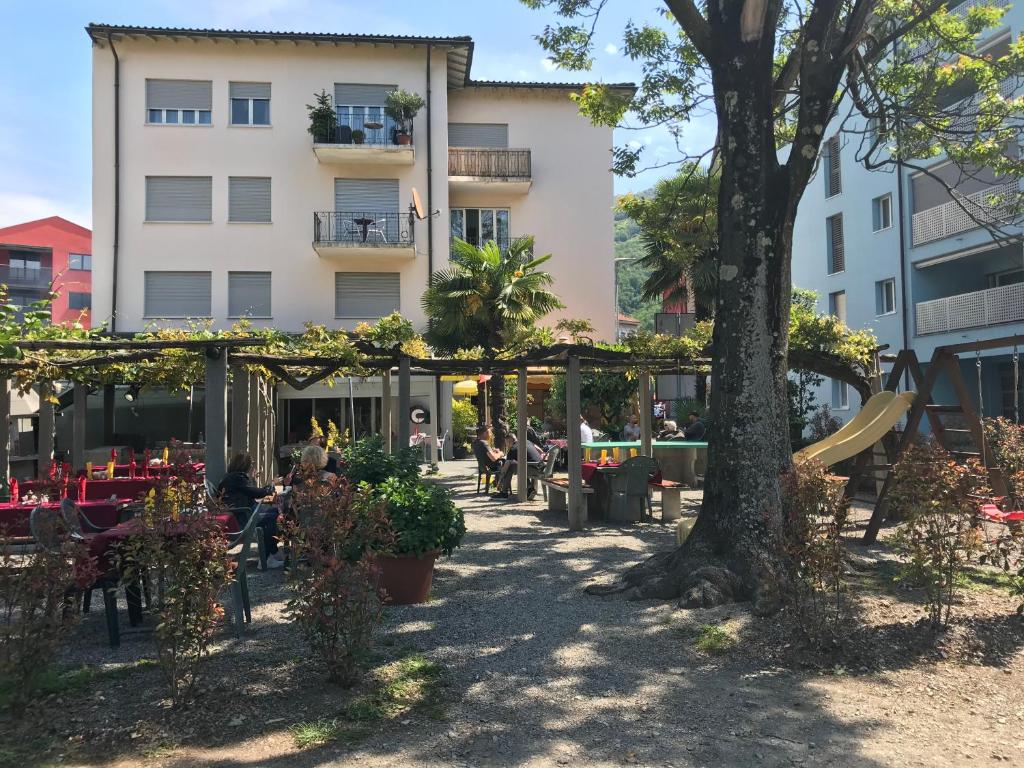 un parque con un árbol y sillas y un edificio en Hotel San Giobbe, en Giubiasco