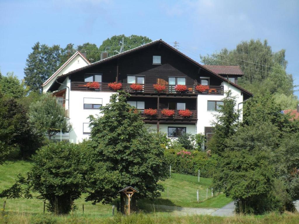 Un grand bâtiment blanc avec des fleurs rouges sur les balcons dans l'établissement Ferienpension Fremuth, à Ruhmannsfelden