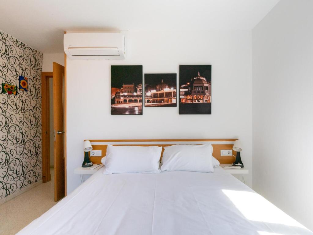 a bedroom with a white bed with four paintings on the wall at Apartamento LABORT in Cádiz