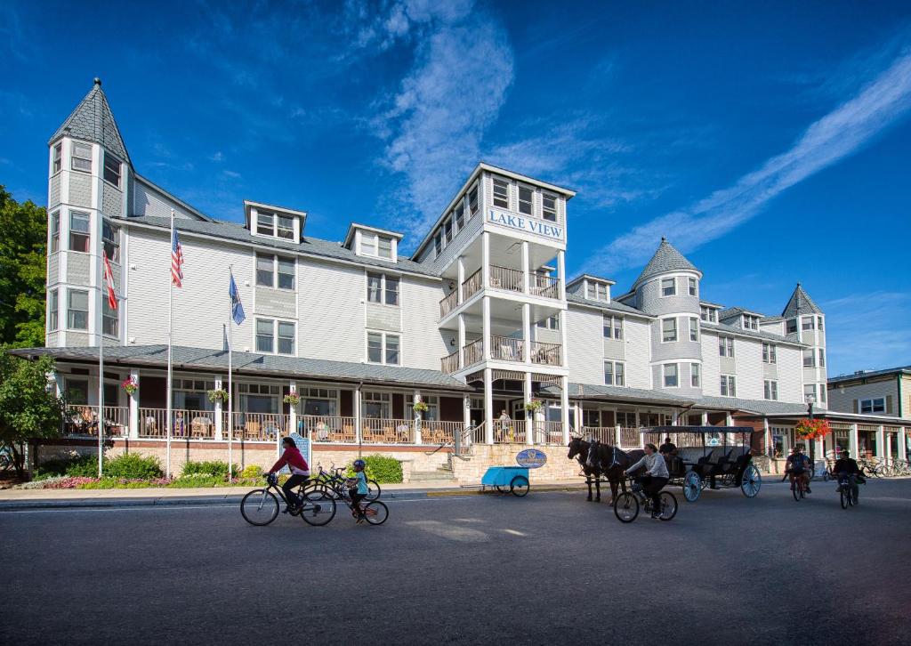 um grupo de pessoas a andar de bicicleta em frente a um grande edifício em Lake View Hotel em Mackinac Island