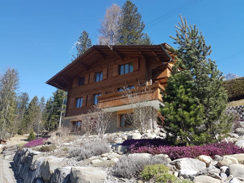 a large wooden house on a hill with flowers at Chalet Grüneggli in Adelboden