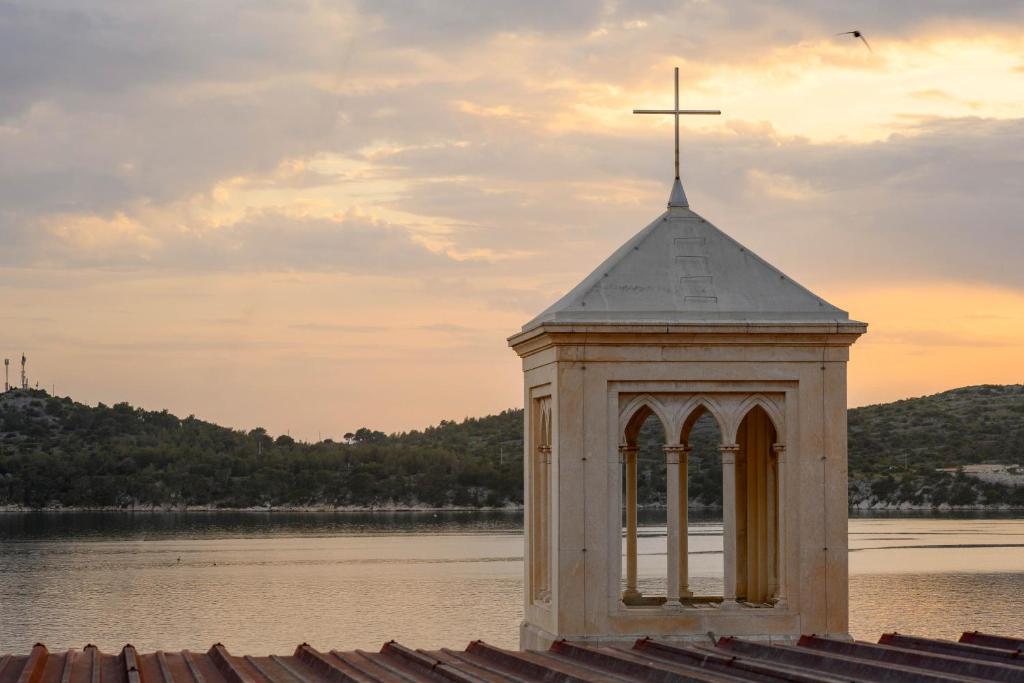 a small church with a cross on top of the water at On the Rock Apartments in Šibenik