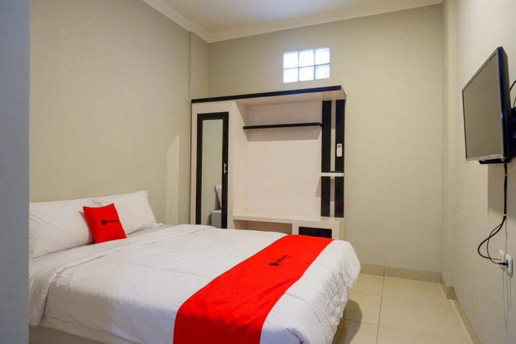 1 dormitorio con cama blanca y almohada roja en RedDoorz Plus near Jogja City Mall 5, en Yogyakarta