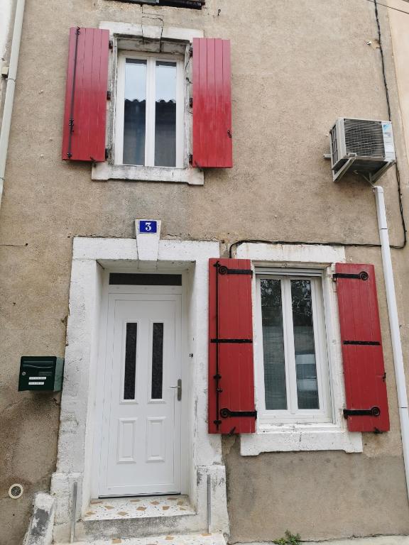 a building with red shutters and a white door at Gîte du ruisseau in Nissan-lez-Enserune