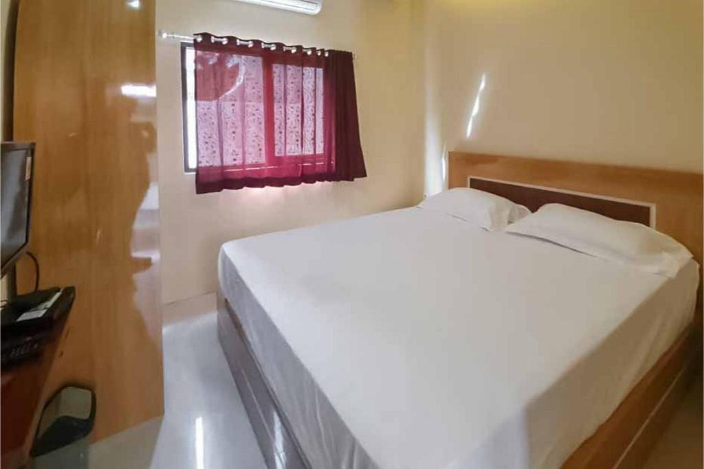1 cama blanca en un dormitorio con ventana roja en Jatiwangi Syariah Guest House Mitra RedDoorz en Majalengka
