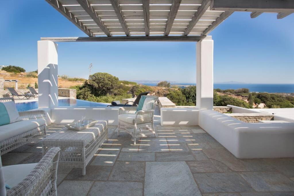 een patio met witte meubels en uitzicht op de oceaan bij Infinity Blue in Kampos Paros
