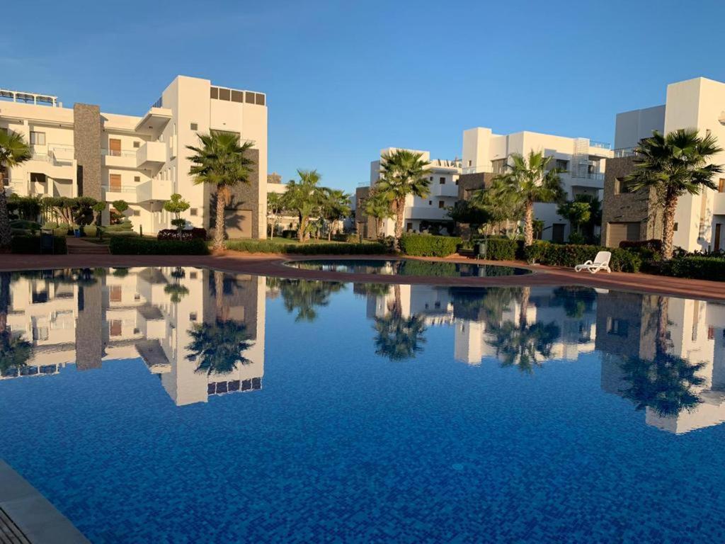 une grande piscine avec des palmiers et des bâtiments dans l'établissement Appartement perla saidia, à Saïdia