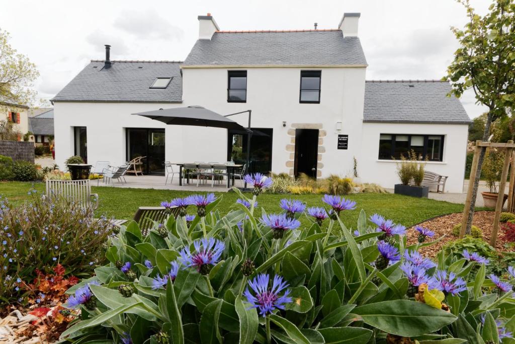 une maison blanche avec des fleurs violettes dans la cour dans l'établissement La maison de Jean, à Milizac