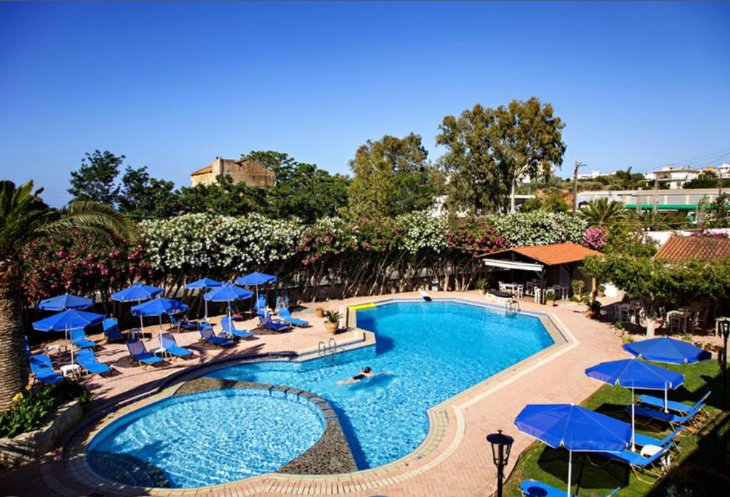 a swimming pool with blue umbrellas and lounge chairs at Lili Apartments,oasis 2,5 km from Hania center in Parigoría