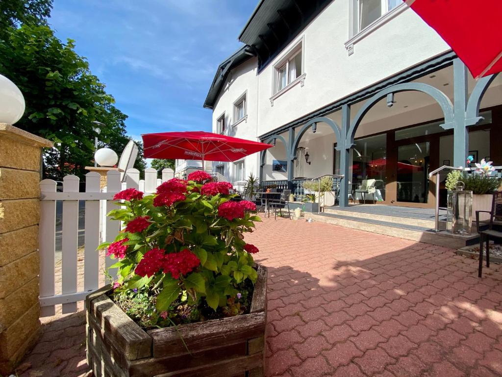 un patio con una sombrilla roja y flores rojas en Hotel Altes Kurhaus, en Baabe