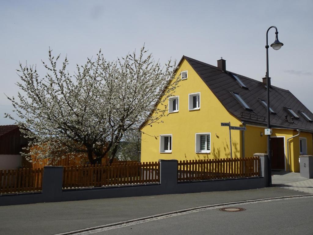 a yellow house with a black roof and a fence at Fichtelhaisla in Röslau