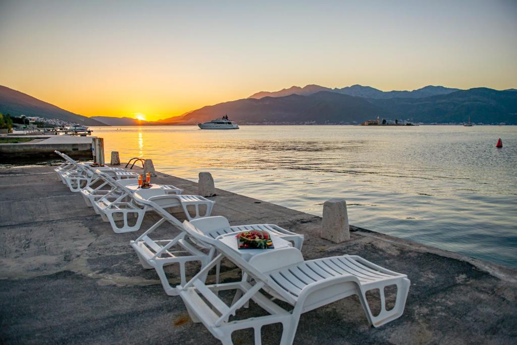 a row of white chairs sitting on a dock near the water at Apartments Dragojević in Tivat