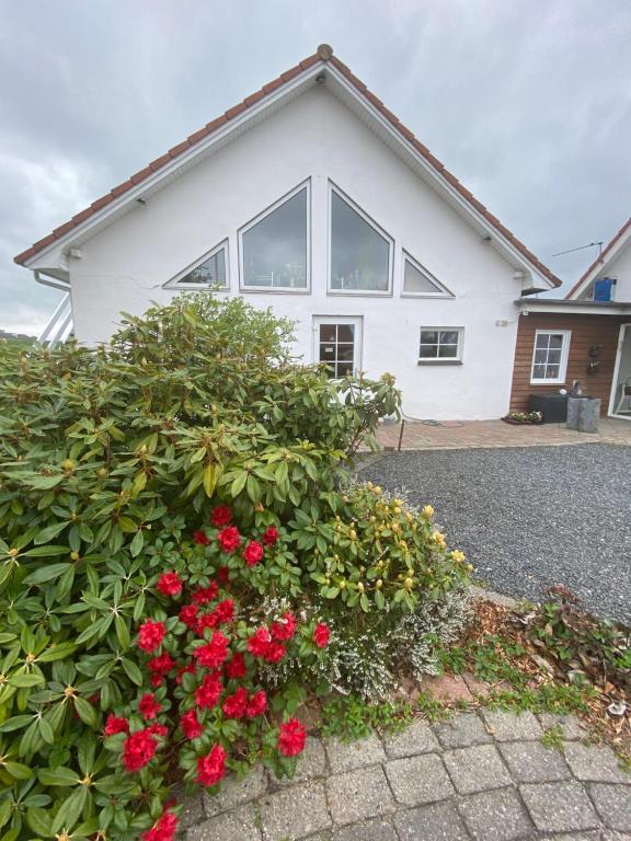 una casa blanca con flores rojas delante en Margretelyst Ferielejlighed en Farsø