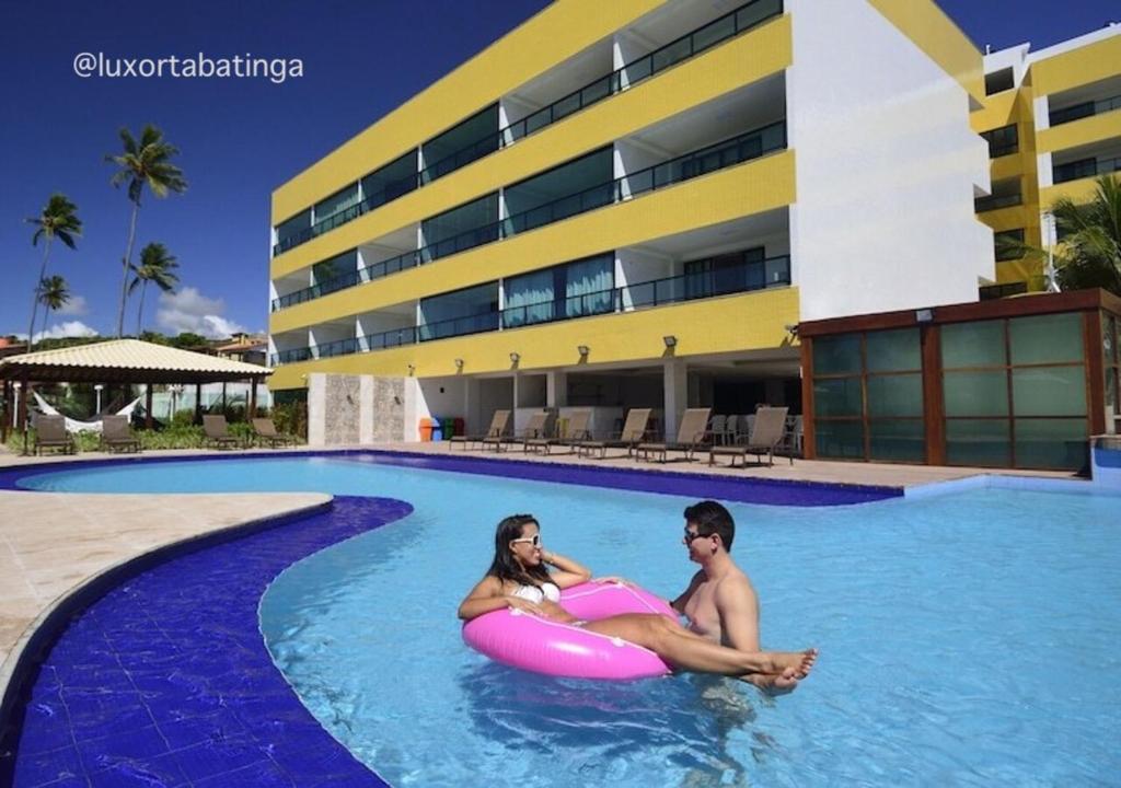 two people are sitting on an inner tube in a swimming pool at Luxor Tabatinga Beira Mar in Conde