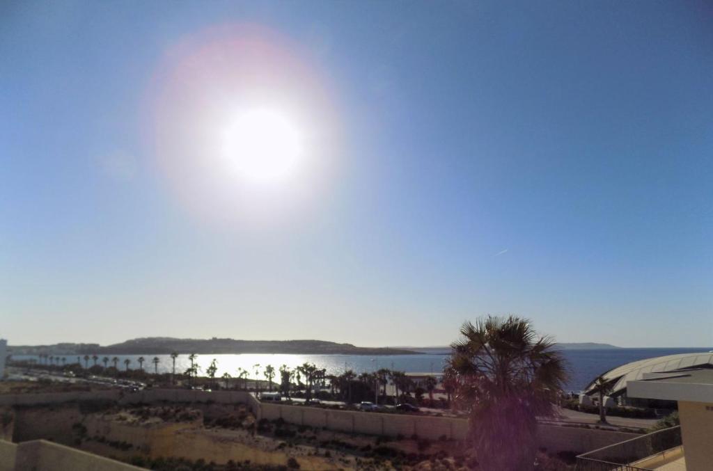 Elle offre une vue sur une plage avec un palmier et le soleil. dans l'établissement Sunshine Holiday Apartment 5 with Spectacular Seaviews, à San Pawl il-Baħar