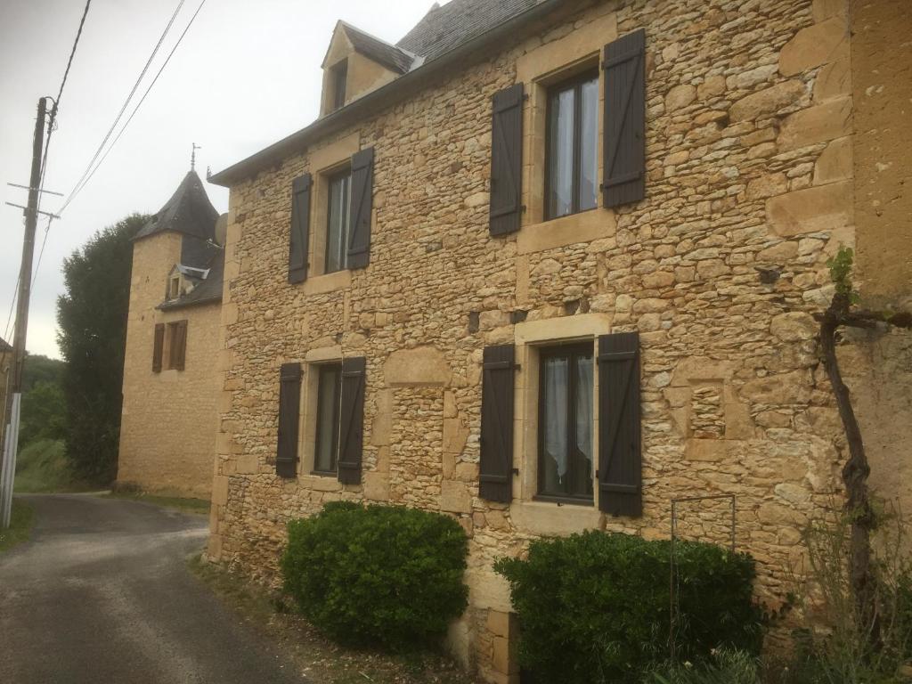 ein altes Steinhaus mit schwarzen Rollläden auf einer Straße in der Unterkunft Maison 5 pièces dans hameau pittoresque très calme in Payrac