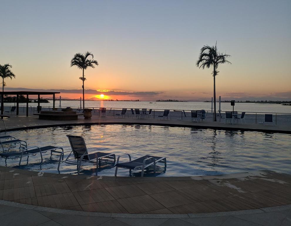 阿拉亞爾多卡博的住宿－GOLDEN LAKE RESIDENCE ARRAIAL DO CABO，日落时分带椅子和棕榈树的游泳池