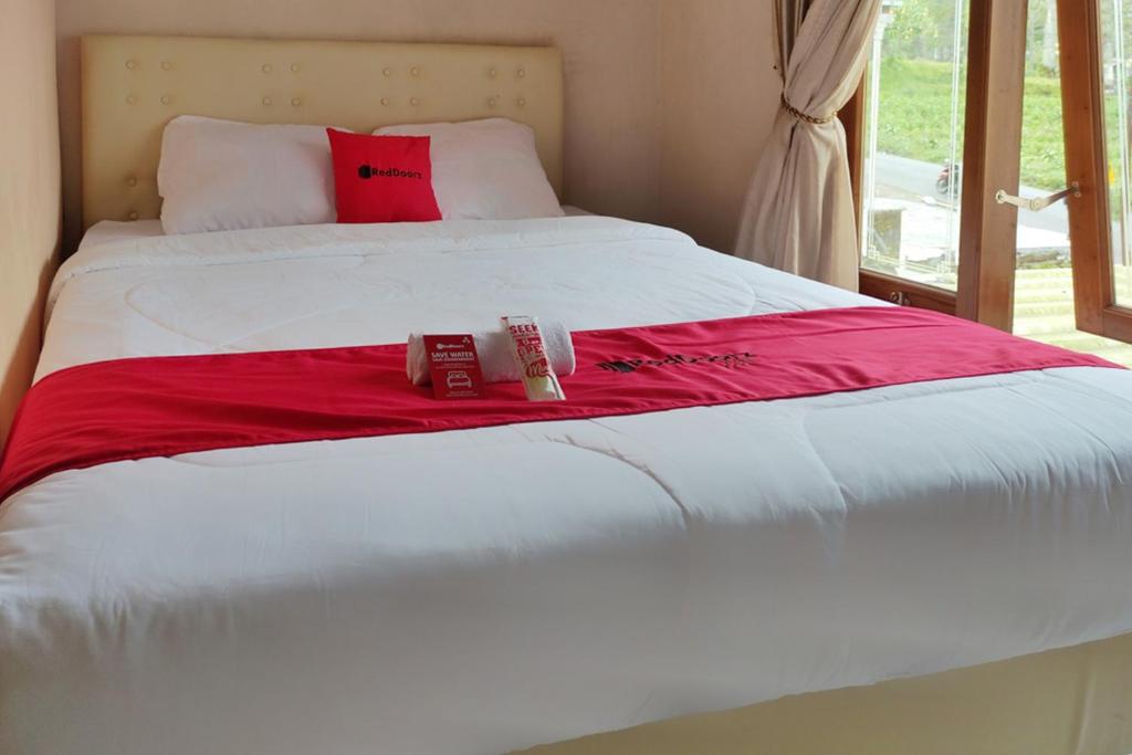 uma cama branca com um cobertor vermelho e duas caixas. em RedDoorz near Agrowisata Kebun Teh Dieng em Wonosobo