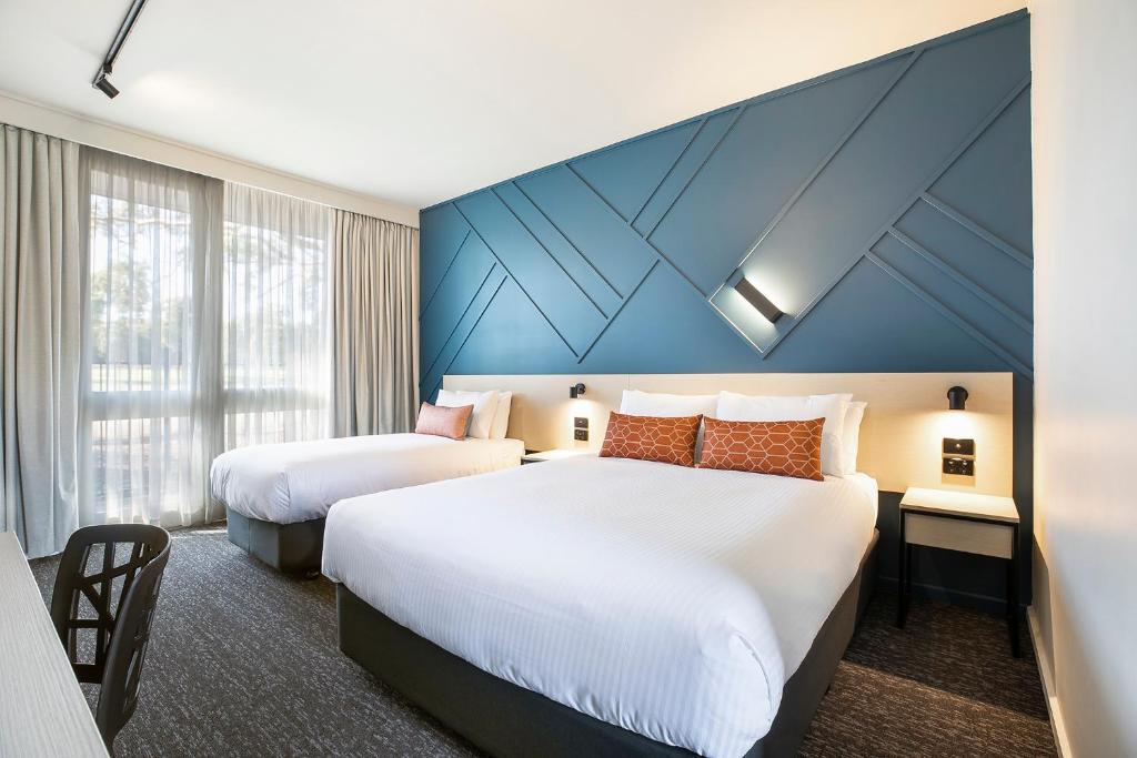 um quarto de hotel com duas camas e uma parede azul em Nightcap at Sandown Park Hotel em Noble Park