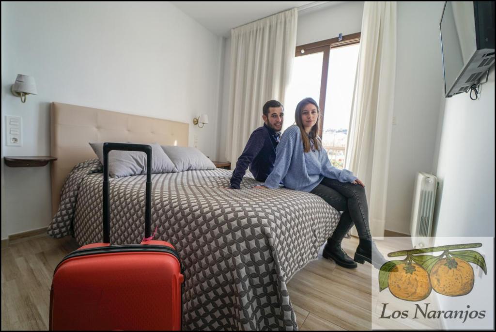 a man and woman sitting on a bed with luggage at Hostal y Apartamento Rural Los Naranjos in Melegis