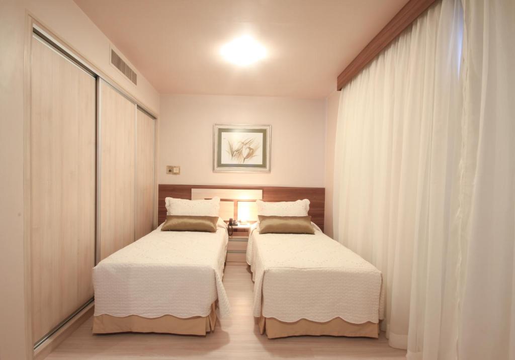 twee bedden in een kamer met witte muren en gordijnen bij Le Premier Apartamentos in Sao Paulo