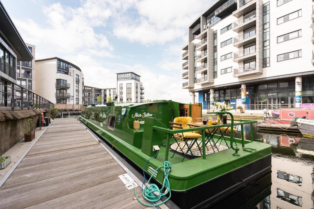 a green boat parked next to a dock with buildings at The Four Sisters Boatel - Houseboat in Edinburgh