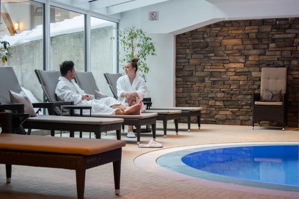 a man and woman sitting in chairs next to a swimming pool at Walliserhof Grand-Hotel & Spa Relais & Châteaux in Saas-Fee