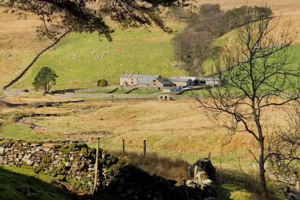 a farm with a stone wall in a field at Kingsdale Head Cottage in Weathercote