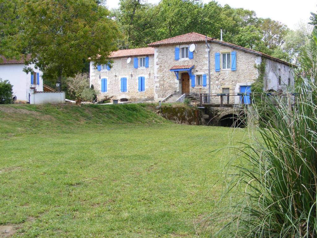 ein altes Steinhaus mit blauen Fenstern auf einem Feld in der Unterkunft Gîte du Moulin in Gamarde-les-Bains