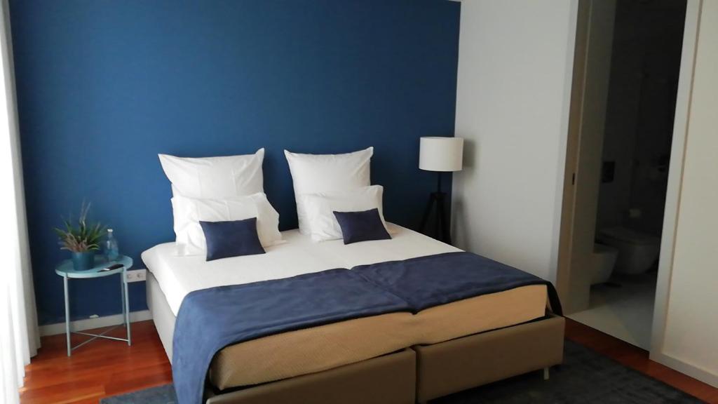 een slaapkamer met een groot bed met een blauwe muur bij Maia Centro in Maia