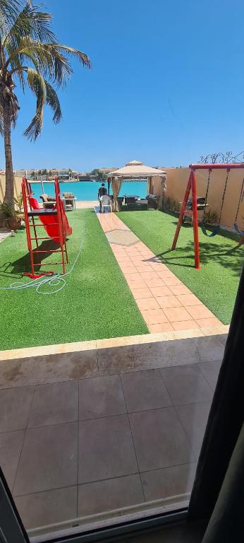 eine rote Bank auf dem Gras in der Nähe des Ozeans in der Unterkunft درة العروس كورال بيتش فيلا in Durrat Al-Arus