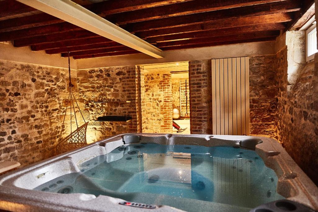 a large bath tub in a room with a stone wall at Demeure de Manneville - SPA - 1Km des plages de Cabourg in Dives-sur-Mer