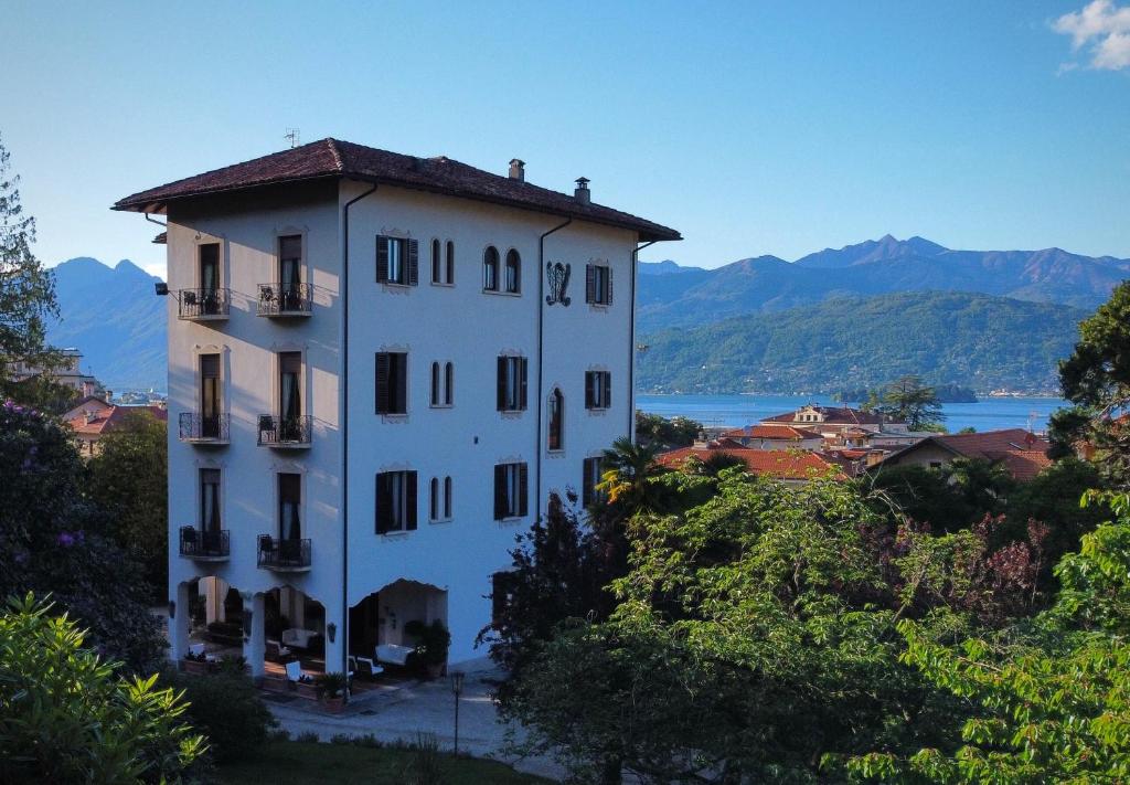 a white building on a hill with mountains in the background at Hotel Du Parc in Stresa