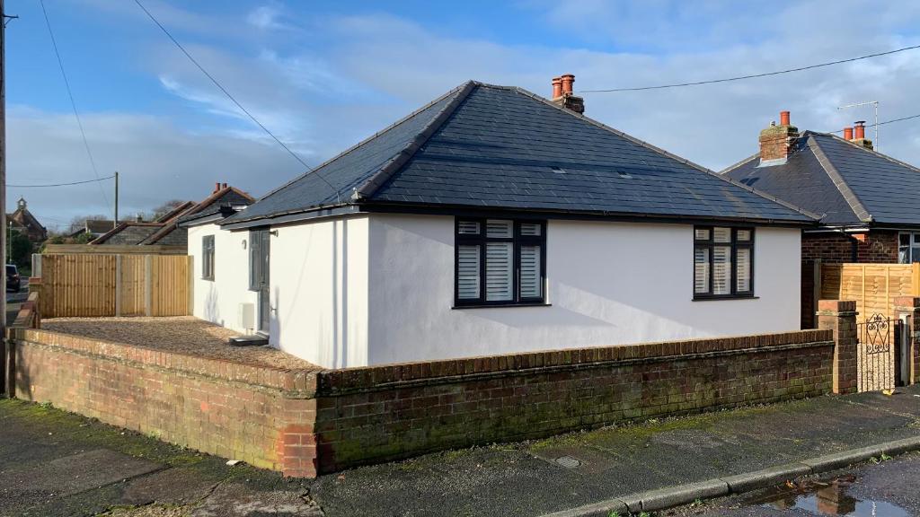 a white house with a black roof and a brick wall at Cosy Corner in Littlehampton