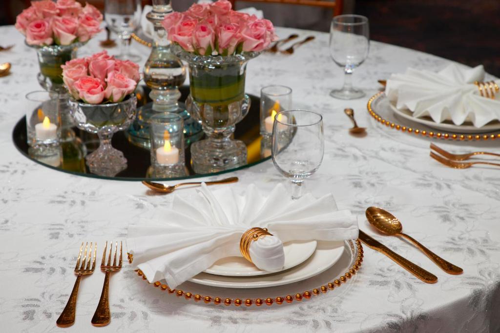 a table with a white table cloth with flowers and silverware at Royal Tulip Muscat in Muscat