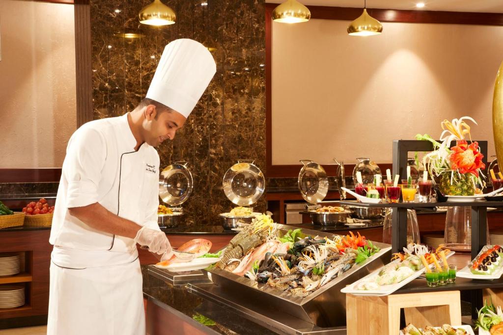 a chef preparing food in a restaurant kitchen at Royal Tulip Muscat in Muscat