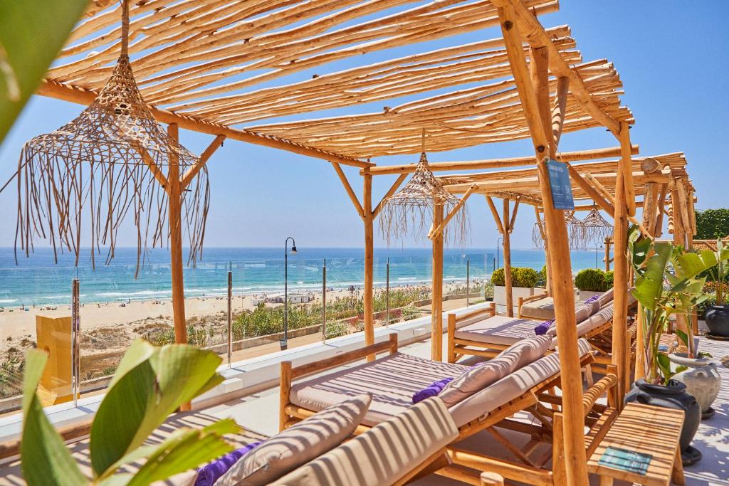 a group of lounge chairs under a wooden pavilion at the beach at FERGUS Conil Park in Conil de la Frontera