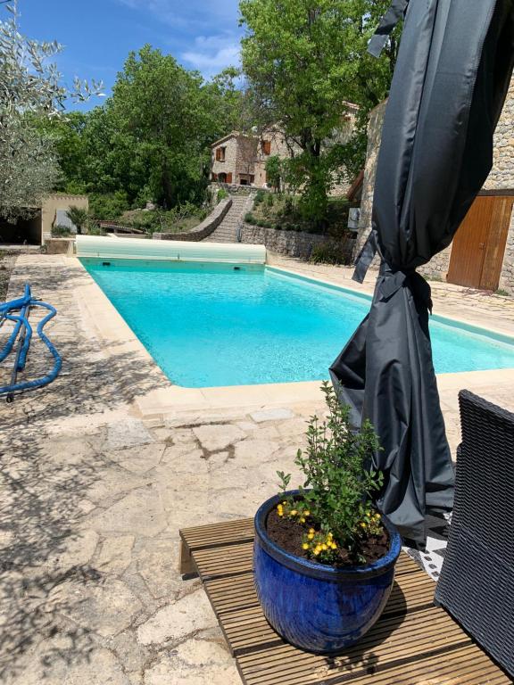ein großer Regenschirm auf einem Tisch neben einem Pool in der Unterkunft FONT NOUVELLE maison de charme Drôme Provençale, 6 ou 10 personnes avec piscine in Plaisians