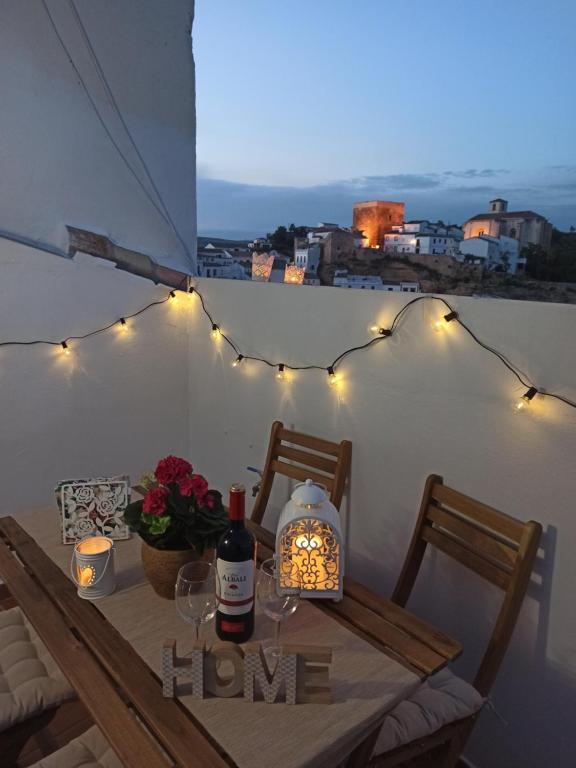 una mesa con copas de vino y luces en el balcón en Casa Rural Abril, en Setenil