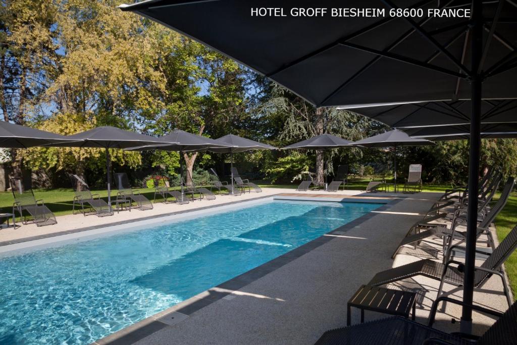 a large swimming pool with umbrellas and chairs and a pool at Aux Deux Clefs Hostellerie Groff in Biesheim