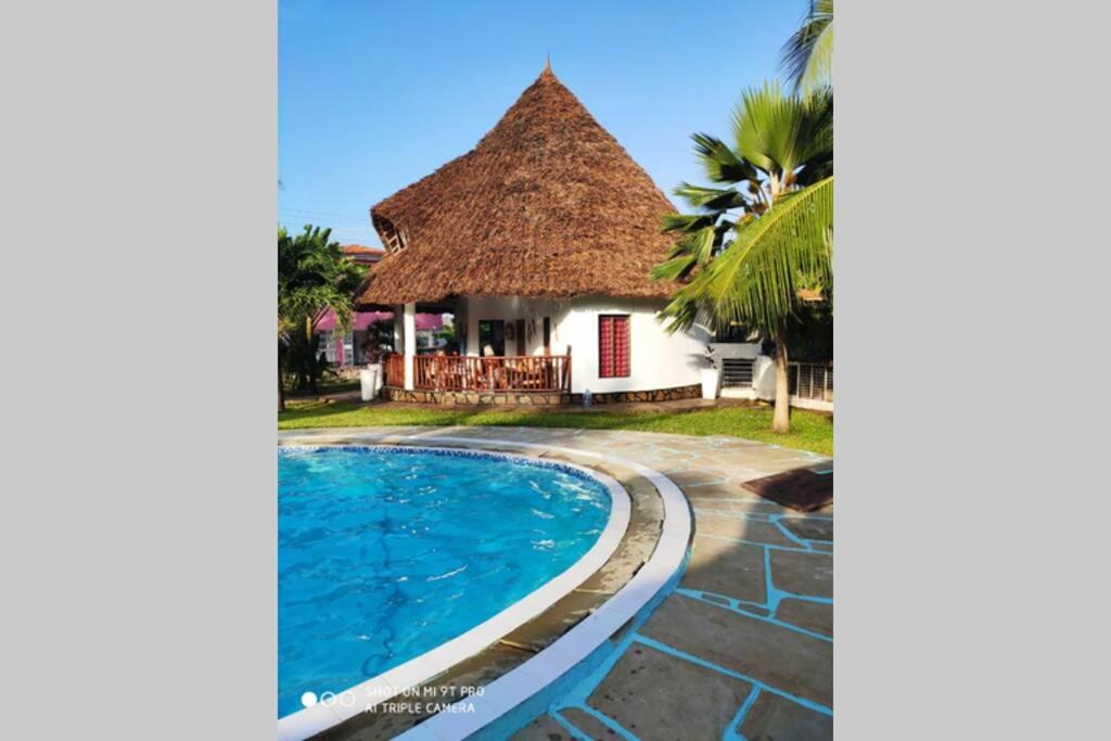 a villa with a pool and a thatch roof at Dadida‘s Pool Cottage in Diani Beach