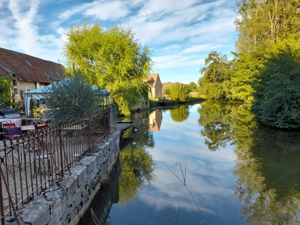 a river with trees and buildings and a blue sky at Le Moulin de Gâteau in Saint-Pierre-les-Étieux