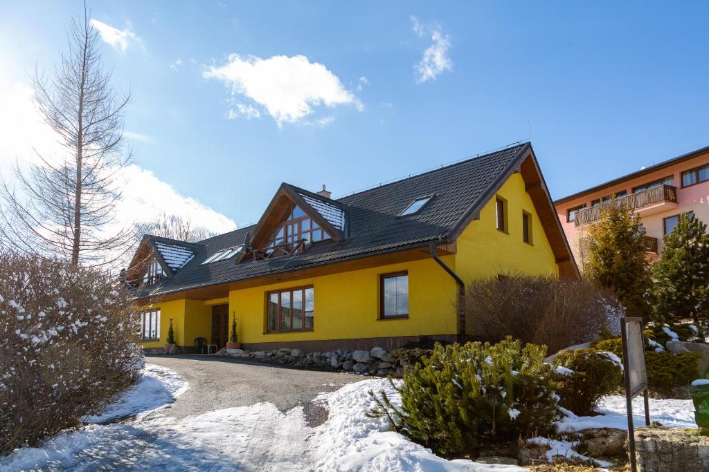 een geel huis met een zwart dak in de sneeuw bij Apartmány Snežienka in Nový Smokovec