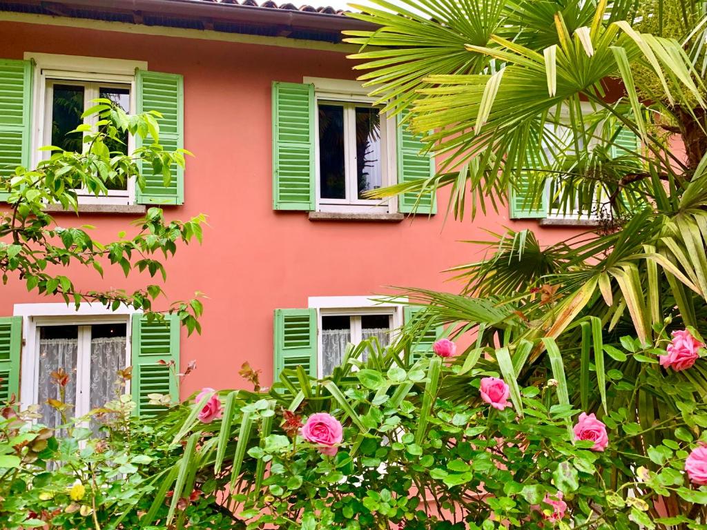 a pink building with green shuttered windows and flowers at Il Giardino Segreto Arona, Charming Apartments in Arona