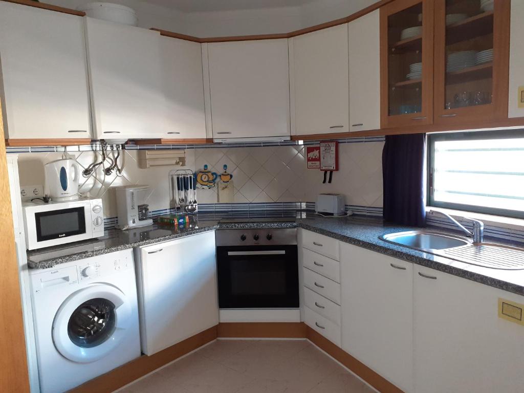 a small kitchen with white cabinets and a dishwasher at Clube Meia Praia in Lagos