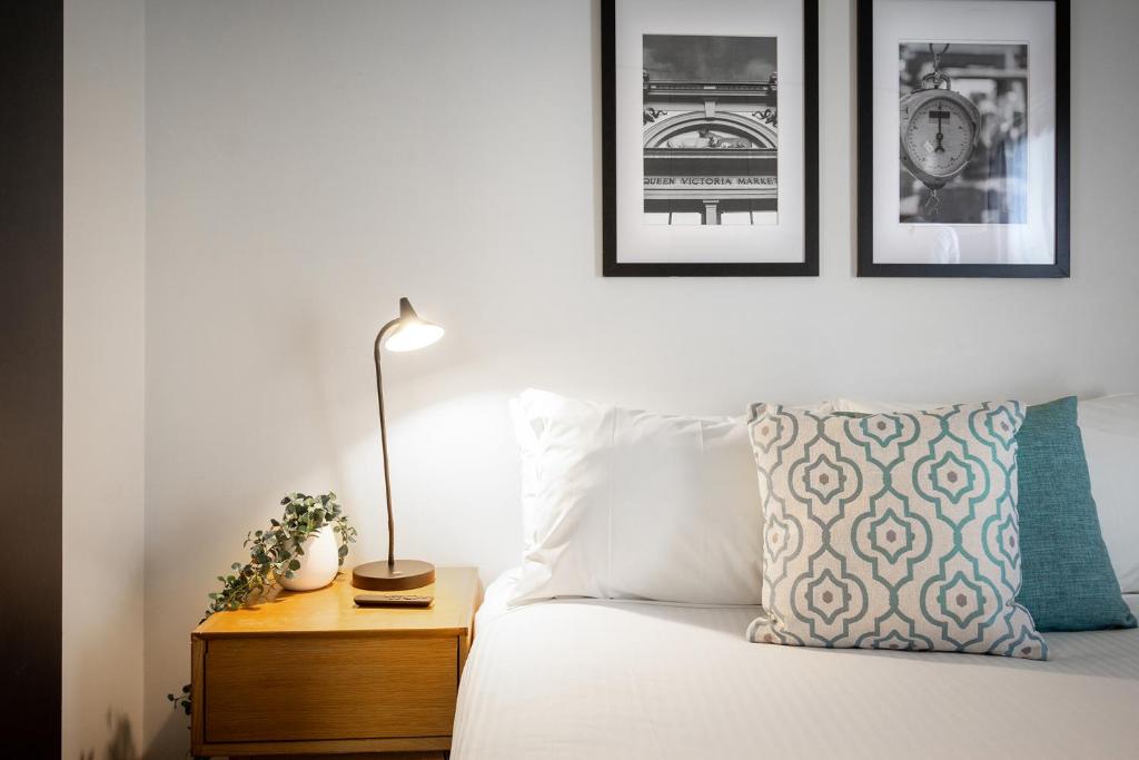 um quarto com uma cama com um candeeiro e fotografias na parede em City Edge North Melbourne Apartment Hotel em Melbourne