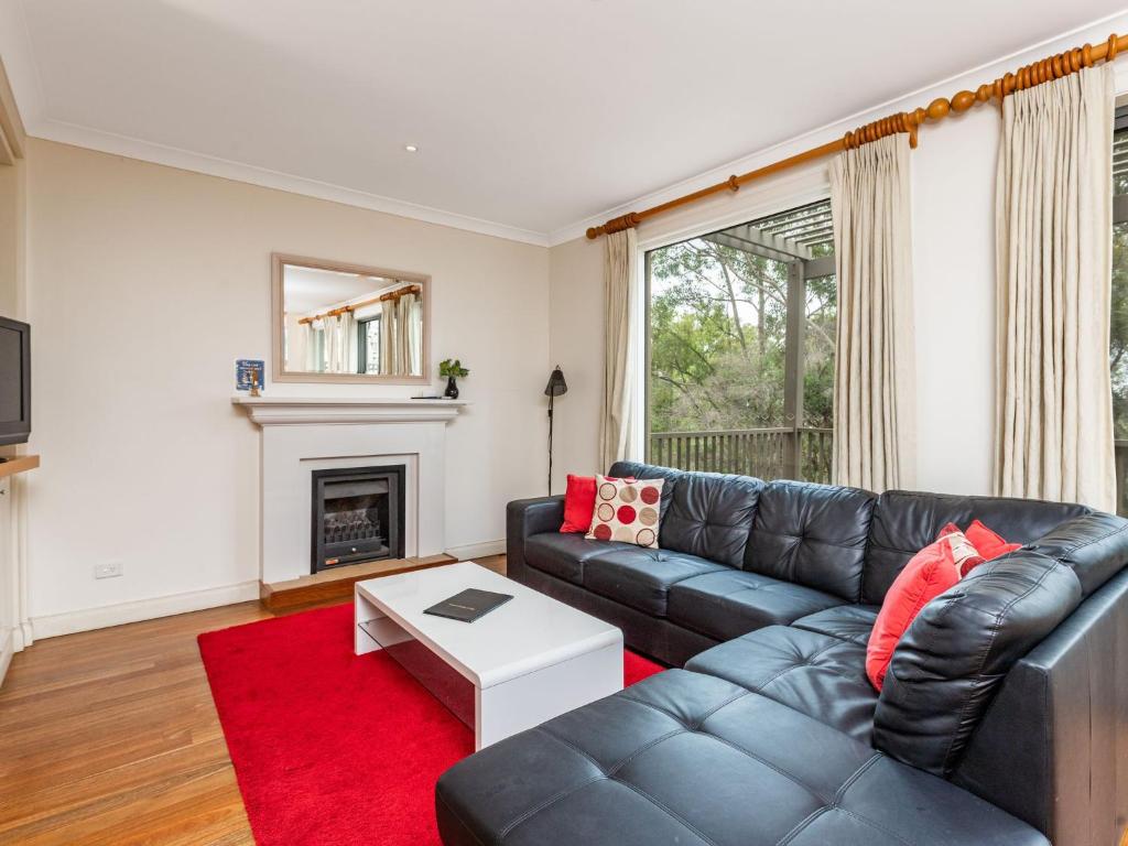 sala de estar con sofá de cuero negro y alfombra roja en Villa 2br Riesling Villa located within Cypress Lakes Resort, en Pokolbin