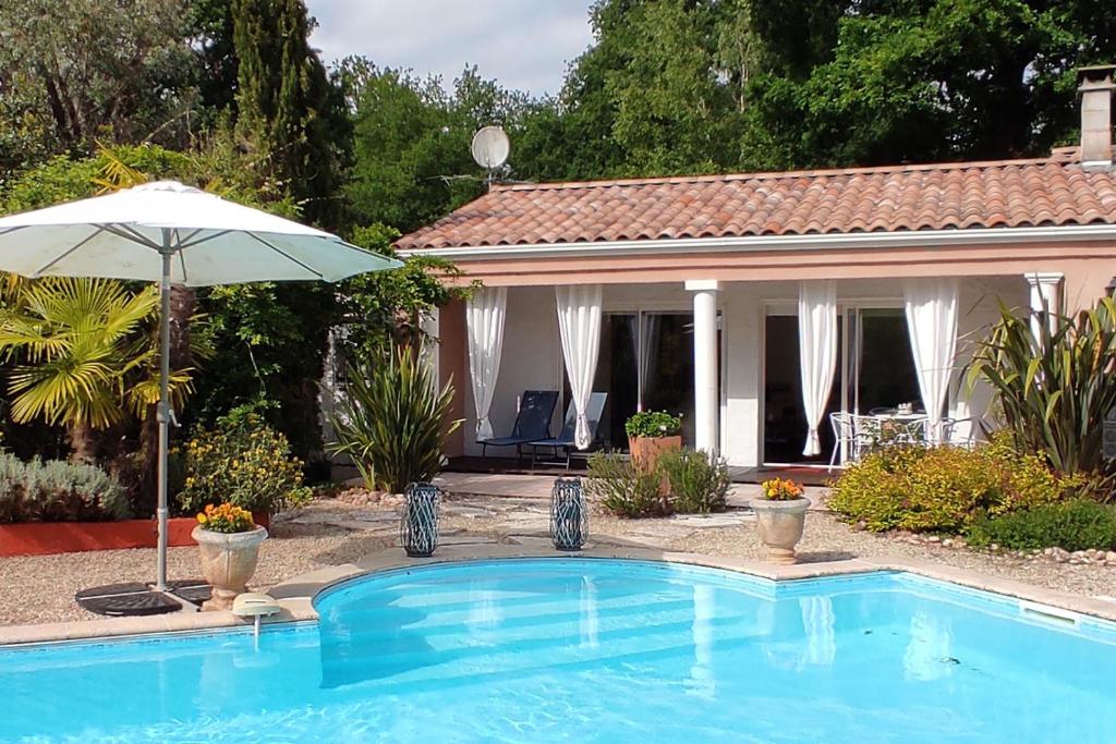 a swimming pool with an umbrella and a house at Sur la route des châteaux du Médoc in Blanquefort